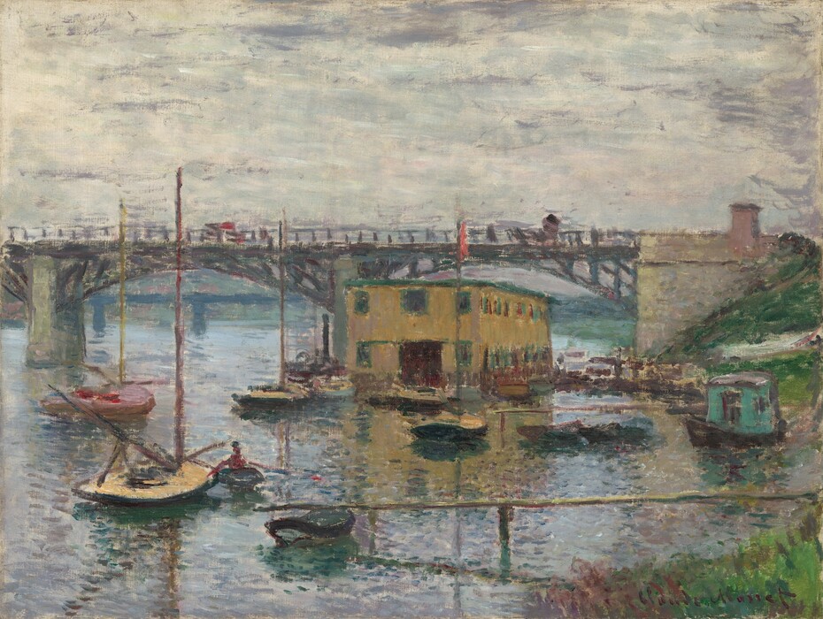 We look across a glimmering river toward docks, about a dozen small boats, and a mustard-brown, boxy building under a bridge that crosses the width of the canvas in this horizontal landscape painting. A patch of green grass lines the riverbank in the lower right corner of the canvas. The land curves away out of sight, and then back into the scene below the abutment of the bridge along the right side of the painting. From the ivory-colored abutment, the straight deck of the bridge is supported by two shallow, iron-gray arches, and the bridge extends off the left side of the composition. Dots of red and gray on the bridge suggest vehicles or pedestrians. The river below is painted with blended strokes of silvery gray, icy blue, and pale lavender purple around the low-sided sailboats. One turquoise-colored houseboat is pulled up to the riverbank to our right. The long, rectangular, flat-topped building is pierced with two stories of windows, which are outlined in spruce green against the golden yellow. The horizon line runs just below the bridge deck, just under halfway up the composition. The sky above is painted with longer swipes of cream white and smoke gray. Loose, short brushstrokes are visible throughout, especially in the water, boats, and bridge. The artist signed the painting in the lower right corner, "Claude Monet."