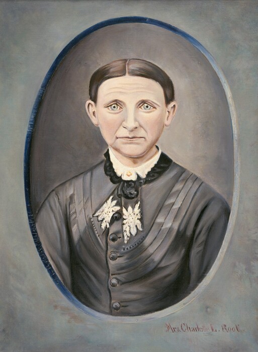 The image depicts a portrait of a person looking directly at the viewer. The person has distinct facial features, light-colored eyes, and a neutral expression. They have dark hair, parted in the middle and combed back, revealing the forehead. The person is wearing a dark-colored garment with decorative elements like buttons, textured design on the shoulders, lace or floral embellishment at the collar, and a black bow above it. The high-neck garment has a plain background with a circular frame around the portrait, appearing oval-shaped with a gradient effect towards the edge. At the bottom right corner, there is a signature or name that reads "Mrs. Charles L. Root."