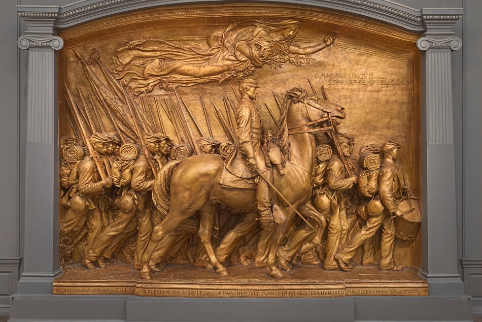 A white man in military uniform rides a horse in front of a regiment of five rows of Black troops in this sculpture, which is painted entirely in gold. The artist created a shallow, stage-like space with an arched top so the men are sculpted in three dimensions, though they become more compressed as they move back in space. The men and horse face our right in profile in this view. The man on the horse has a pointed, straight nose and a goatee. He wears a cap with a flat top and narrow brim, a knee-length coat, gloves, and knee-high boots with spurs. He holds a thin sword down by the side of the horse with his right hand and holds the reins of the horse with his left. The horse’s head is pulled upward by the short reins, and its mouth is open around the bit. About twenty soldiers are lined up in rows beyond the horse, and they march in unison. They carry blankets rolled atop knapsacks, canteens, and rifles resting on their right shoulders. However, the details of how their uniforms bunch up around their equipment and the way their caps have been molded and fit is unique to each person. Their ages also vary from young and cleanshaven to bearded, older men. Two men carry furled flags near the back, to our left, and a drummer boy plays at the head of the regiment, to our right. All the men look straight ahead, their lips closed. A woman in a billowing robe floats above them under the arched top of the sculpture with her eyes closed. Her left arm is outstretched, and she holds a laurel branch and poppies close to her body with her right arm. An inscription in the upper right corner is created with raised capital letters: “OMNIA RELINQVIT SERVARE REMPVBLICAM.” A longer inscription is carved into the base along the bottom edge of the memorial, also in all caps: “ROBERT GOVLD SHAW KILLED WHILE LEADING THE ASSVLT ON FORT WAGNER JVLY TWENTY THIRD EIGHTEEN HVNDRED AND SIXTY THREE.” The artist’s signature is inscribed In the lower right corner, in smaller letters: “AVGVTVS SAINT GAVDEN M-D-C-C-C-L X X X X V I I I.”