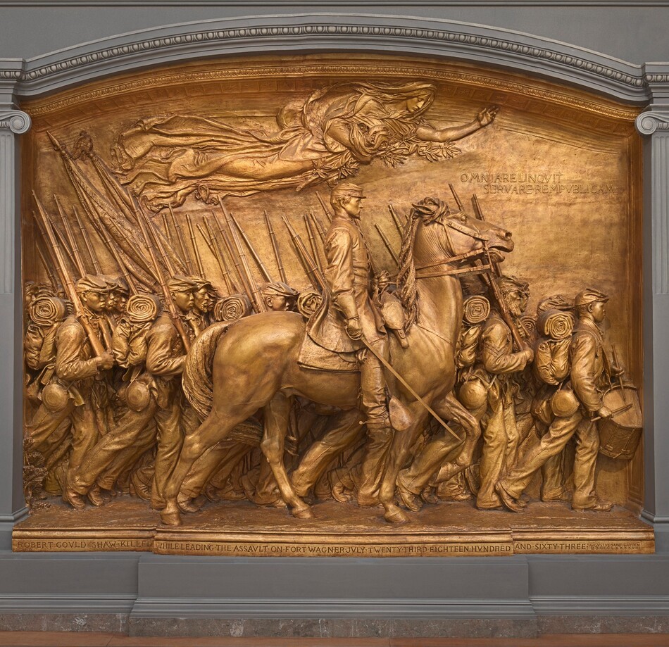 A white man in military uniform rides a horse in front of a regiment of five rows of Black troops in this sculpture, which is painted entirely in gold. The artist created a shallow, stage-like space with an arched top so the men are sculpted in three dimensions, though they become more compressed as they move back in space. The men and horse face our right in profile in this view. The man on the horse has a pointed, straight nose and a goatee. He wears a cap with a flat top and narrow brim, a knee-length coat, gloves, and knee-high boots with spurs. He holds a thin sword down by the side of the horse with his right hand and holds the reins of the horse with his left. The horse’s head is pulled upward by the short reins, and its mouth is open around the bit. About twenty soldiers are lined up in rows beyond the horse, and they march in unison. They carry blankets rolled atop knapsacks, canteens, and rifles resting on their right shoulders. However, the details of how their uniforms bunch up around their equipment and the way their caps have been molded and fit is unique to each person. Their ages also vary from young and cleanshaven to bearded, older men. Two men carry furled flags near the back, to our left, and a drummer boy plays at the head of the regiment, to our right. All the men look straight ahead, their lips closed. A woman in a billowing robe floats above them under the arched top of the sculpture with her eyes closed. Her left arm is outstretched, and she holds a laurel branch and poppies close to her body with her right arm. An inscription in the upper right corner is created with raised capital letters: “OMNIA RELINQVIT SERVARE REMPVBLICAM.” A longer inscription is carved into the base along the bottom edge of the memorial, also in all caps: “ROBERT GOVLD SHAW KILLED WHILE LEADING THE ASSVLT ON FORT WAGNER JVLY TWENTY THIRD EIGHTEEN HVNDRED AND SIXTY THREE.” The artist’s signature is inscribed In the lower right corner, in smaller letters: “AVGVTVS SAINT GAVDEN M-D-C-C-C-L X X X X V I I I.”