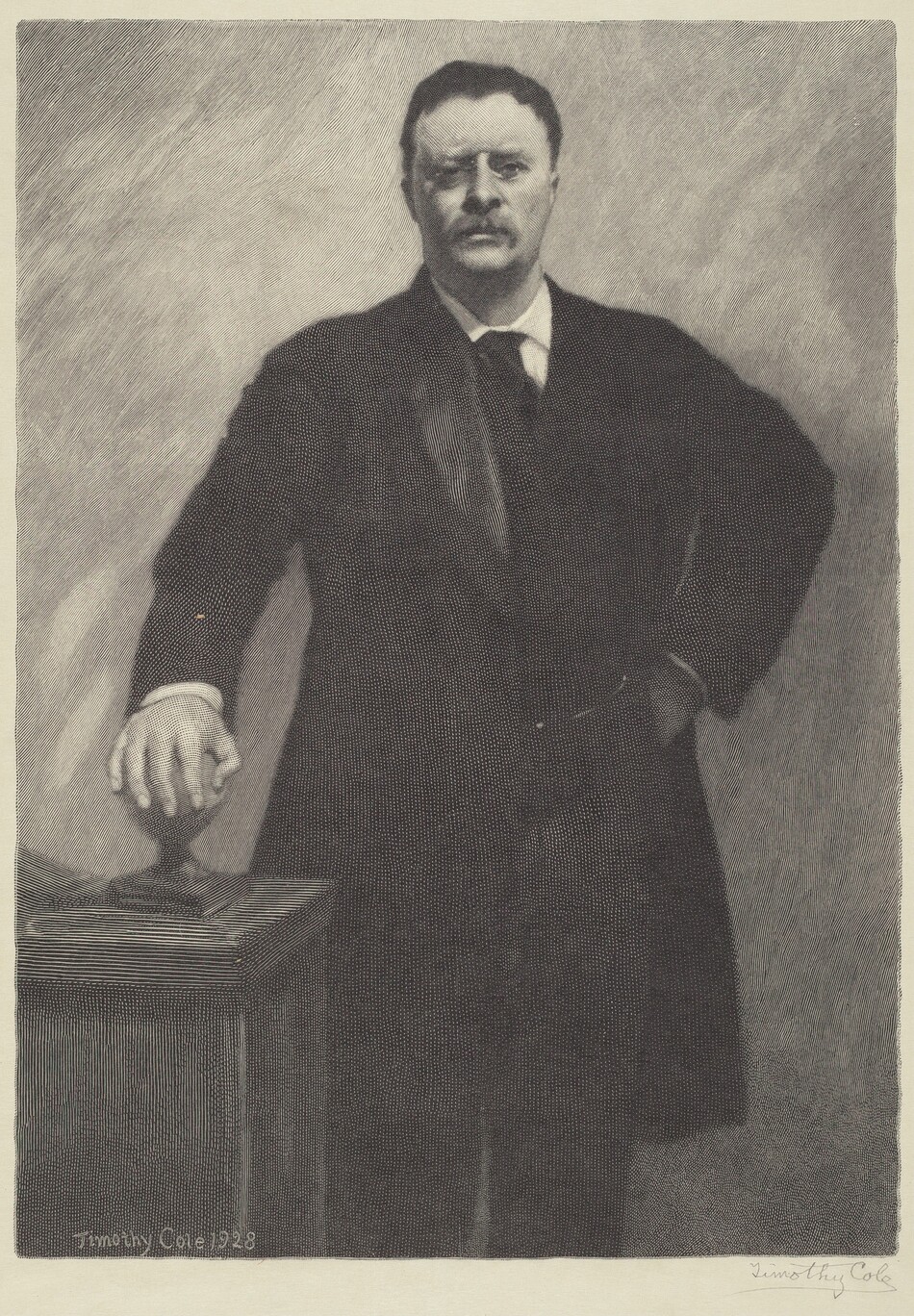 The image shows a man standing with one hand resting on a piece of furniture and the other hand on his hip. He has a bushy mustache, neatly combed back hair, and is wearing a dark suit with a white shirt and a dark tie. He wears small, round glasses on his nose. The background has a simple textured pattern.