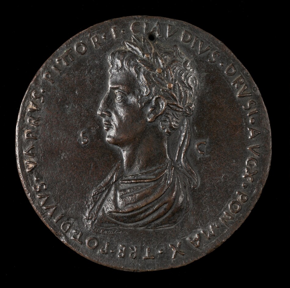 The image depicts a relief sculpture of a profile of a classical Roman figure, likely a man, wearing a laurel wreath. The subject is depicted with a detailed hairstyle and distinct facial features, giving a realistic impression. The sculpture is set on a round medallion or coin-like object. It is made of dark metal, probably bronze, with a slightly weathered yet smooth surface and a brownish patina. The sculpture is approximately life-sized in relation to the medallion's diameter, showing the figure's attire and wreath detailing. An inscription in raised lettering surrounds the edge of the medallion.