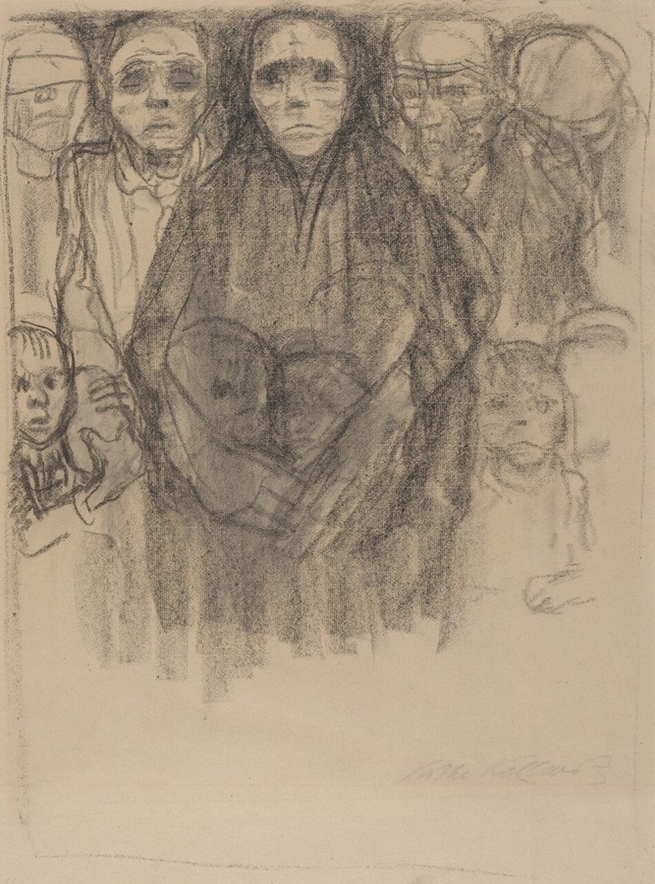Drawn loosely with black charcoal on tan paper, this vertical sheet shows a tightly packed group of hollow-eyed, emaciated adults and children. Four men, a woman, and at least five children fill the top two-thirds of the paper, their heads nearly brushing the top edge. They all stand facing us, their mouths downturned. Dark lines and smudges suggest gaunt faces and deep-set eyes. One man on the far left has a bandage over his eyes. The men wear loose shirts, and two wear caps. The men flank a woman who stands before them in the center, looking out with shadowed eyes. She wears a dark robe with the hood pulled up. Her long arms and oversized hands are wrapped around three children gathered in front of her while two others huddle on either side. One wide-eyed child with mouth agape stands to our left, holding the forearm of the man there with both hands. The woman’s torso fades into broad, vertical charcoal strokes below the waist and a lopsided, thin border encloses the scene. The artist signed the lower right, “Kathe Kollwitz.”