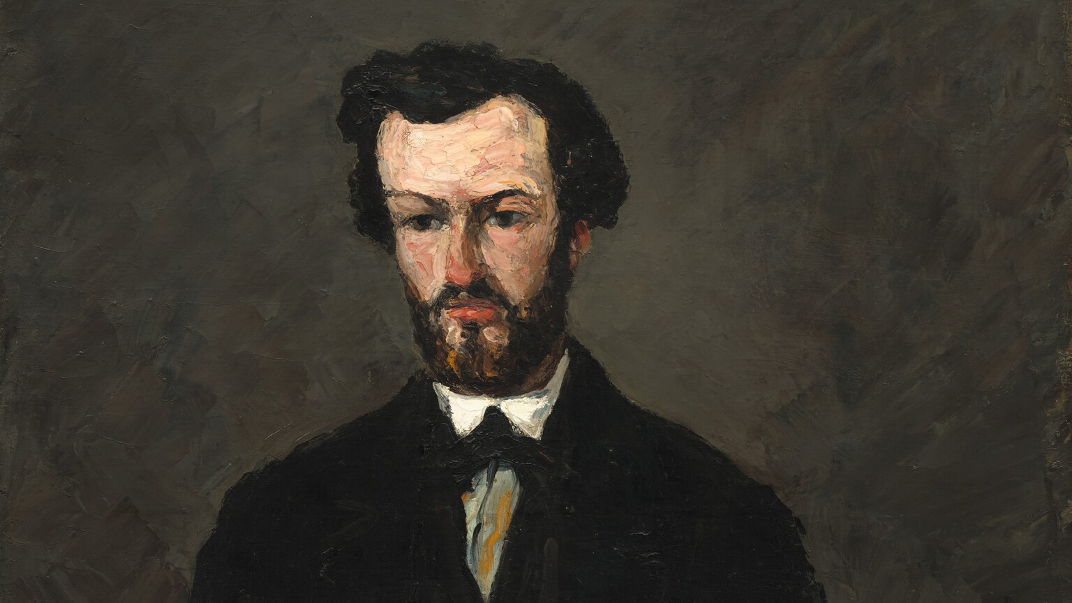 A light-skinned man with thick black hair and a squared off black beard, dressed in a black jacket over a gray vest and gray trousers, sits facing us in this vertical portrait painting. This work is loosely painted with visible brushstrokes so some details are difficult to make out. The man's body faces us but he looks down and to our left. The tip of his nose almost matches the coral red of his lips. Two pale peach patches below his mouth break up his beard on his pointed chin. His hands, closed into fists, rest on his thighs, which are cropped by the bottom of the canvas. He wears several layers of clothing. The open black jacket reveals a charcoal-gray vest with a V-shaped opening over another black garment, perhaps an undervest. This is worn over a white shirt, which is visible as bright traingles at this throat and white cuffs at his wrists. The white shirt seems to be tied with a black tie and possibly a gray cravat, but this area is broadly painted. The background is painted with gray strokes over black. The artist signed the painting in black paint in the lower right corner, though it is barely visible: “P. Cezanne.”