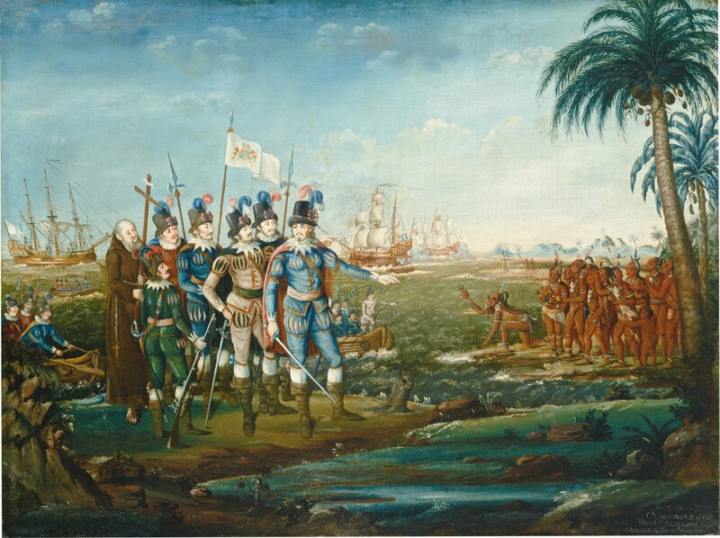 Seven light-skinned men stand closely together at the edge of a body of water across from a group of about a dozen indigenous people with brown skin gathered in the near distance in this horizontal painting. To our left, five of the white men wear tall black hats with blue and pink feathers. In shades of royal blue, parchment white, pine green, or brick red, their caped suits have slashes across the chest, shoulders, and upper thighs. Some hold or wear swords, and most have knee-high, olive-green boots. At the back of the group, a hatless, balding man wears a long brown robe with a rosary and cross hanging from his waist. He holds a tall wooden cross, and the others carry spear-like halberds, a rifle, or a white banner. The man at the front of the group holds a sword down by one side and gestures toward the group of brown-skinned people with his other hand. Two rowboats filled with similarly dressed men approach their position on the left side. Three wooden ships lie in the water beyond the men. The indigenous men, women, and children wear off-white or red loincloths, along with earrings, necklaces, armbands, and anklets. Many have feathers in their dark hair. One person at the front of that group kneels and points toward the water with one hand as he holds out a pineapple with the other. The two groups are separated by a jewel-blue waterway that runs between them. More beach and hazy blue mountains in the deep distance curve toward the center of the composition. The artist signed and dated the painting in the lower left, though the inscription is now incomplete. It reads, “eyer Pin t th January 180.” In the lower right, and inscription reads, “First Landing of C.R COLUMBUS at the Island St SALVADOR South AMERICA the 11th October.”