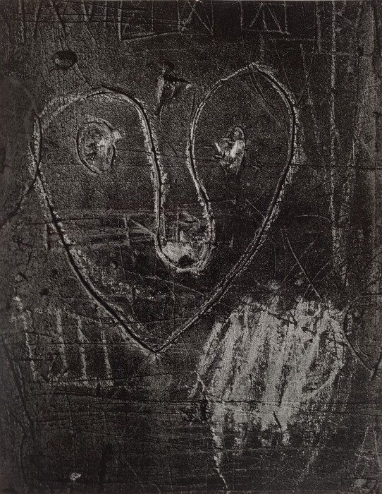 The image depicts an abstract carving with shapes resembling a heart enclosing two circles on a textured surface. The lines and patterns throughout the image evoke hieroglyphs or urban graffiti. The scratched texture adds depth, resembling bark or a cliff face.