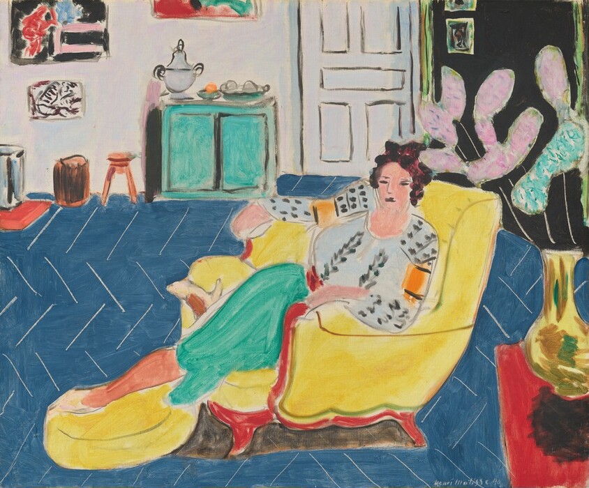 A woman wearing a pale blue and gray patterned top and turquoise skirt stretches out in an armchair in this stylized, almost square painting. The scene is loosely painted with areas of mostly flat color, especially in the background, so some details are difficult to make out. The woman is centered in the composition, and her legs stretch to our left. She has upswept dark brown hair, peach-colored skin, and her eyes, nose, and mouth are drawn with dark gray lines. Her blousy top is vertically patterned with lead-gray leaves down the front and elongated dots on the sleeves. Each sleeve also has a carrot-orange band on the upper arm. Her skirt is spearmint green, and she wears bone-white pumps. She sits in a canary-yellow armchair with red down the front of the arms and along the bottom, where the wood frame would be. One foot stretches to rest on a matching footstool, while her other leg is curled under her. The denim-blue floor tilts toward us and is covered with thin white lines in a chevron pattern. In the lower right is a red table with a bright yellow vase covered with swipes of brown and green. The vase is filled with elongated, abstract mauve-pink and mint-green shapes on slender white stems. The back wall of the room has an aqua-green cabinet to our left, which holds a silver urn and dishes of round objects. There is also a cantaloupe-orange footstool and other pieces of small furniture there, below paintings on the white wall. Above the woman is a white door with panels outlined in gray, and a section of black wall to our right has more paintings. The artist signed and dated the lower right, “Henri Matisse 40.”