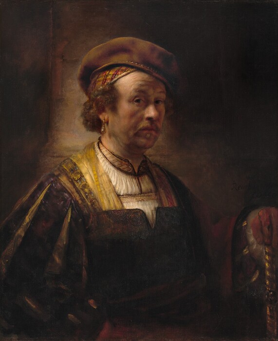 Shown from the waist up, a man dressed in fine clothing looks out at us from against a deeply shadowed background in this vertical portrait painting. The man’s pale, peachy skin has a warm undertone that glows in a stark light source from our left. His body and face are angled to our right, and he cuts his dark eyes back to look at us under raised brows. He has a rounded, bulbous nose, and a wispy golden-brown goatee frames his closed pink lips. Shadows on his cheeks and jowls suggest soft flesh and a five o’clock shadow. Wiry brown hair curls out over his temples and down to the nape of his neck beneath a green, gold, orange, and burgundy-red skullcap. A soft brown beret rests on top of his skullcap tipped at an angle away from us. A teardrop-shaped pearl earring hangs from a gold setting in the ear we can see. He wears a cream-white tunic with gold and brown detailing along the hemlines. Over that is a dark brown, vest-like garment. The sleeves are slashed so the outer fabric is eggplant purple, and the inner slashes are golden yellow. A red cloth drapes over his left arm, farther from us, and that hand rests on a gold, spiraling shaft. A dark sash may be tied around his waist, and it seems that his other hand rests against his hip, to our left. The lower half of his chest and the background fall into deep shadow, though, so some the details there are difficult to make out. The painting is signed and dated in dark letters in a shaded area, so is nearly invisible in the lower center right; it reads, “Rembrandt f. 1650.”