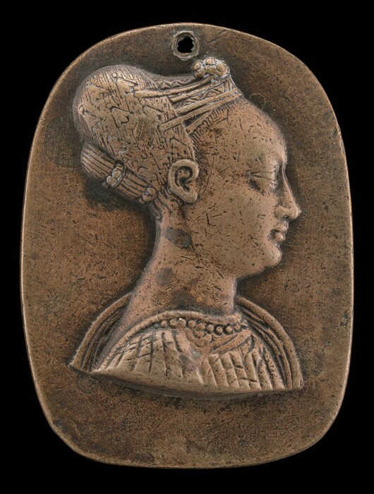 The sculpture is a bas-relief medallion depicting a profile of a woman. Her hair is styled in an updo adorned with intricate patterns, bands, and ornamental elements. The woman is shown in profile facing to the right, with delicate facial features and a smooth complexion. The medallion appears to be made of metal, likely bronze, with a warm brown color and a patina. The portrait of the woman is framed within a rectangular metal plaque with rounded corners, and there is a small hole near the top center. The woman is depicted wearing an elegant attire, with draped fabric around her shoulders, lines, and a beaded necklace.