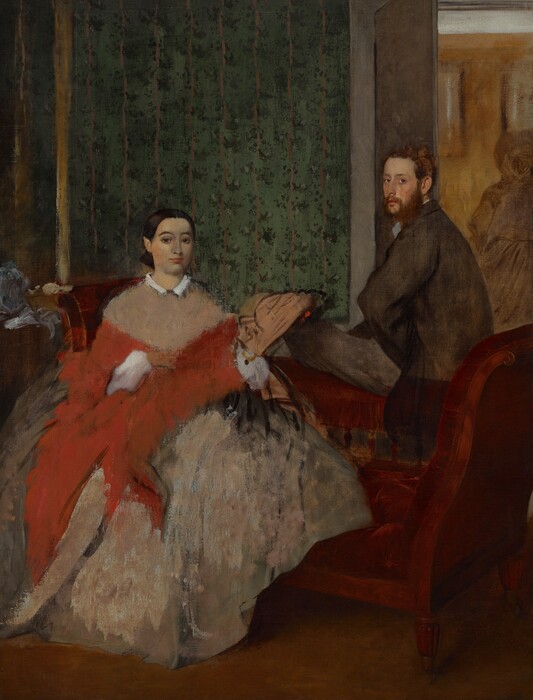 A man and woman, both with pale, peachy skin, sit on opposite sides of a burgundy-red, low-backed sofa in a room wallpapered with a striped, floral pattern in this vertical painting. To our left, the woman sits with her body facing us, and she looks at us with dark eyes under dark, arched brows. She has an oval face, a straight nose, and her coral-pink lips are closed. The woman’s dark brown hair is parted down the middle, and smoothed and pulled back to the base of her head. Her pinkish-tan dress has a narrow white collar and a full, billowing skirt. A loosely painted, crimson-red shawl wraps around her torso and is pulled over white, puffy sleeves. Also loosely painted, a shell-shaped, tan object to our right could be a fan held in her left hand. To our right and on the far side of the piece of furniture, the man sits on the low back of the chaise-longue, his left knee bent so that thigh, closer to us, rests along the back of the sofa. He turns his face to look at us from the corners of his eyes. He has a rounded nose, and his full, pink lips are closed. He has an auburn-brown beard and his short hair is tousled. He wears a brown coat and charcoal-gray slacks. He rests the hand closer to us against his hip so his elbow juts toward us. To either side of the people and nearly spanning the width of the painting, the arms of the chaise curve upward to about the height of the woman’s shoulders. A loosely painted, ball-like form next to the left arm of the chaise could be a hat or other object on a side table. The wall behind the people extends from the left edge of the painting to just behind the man, and is patterned with evergreen-colored dots to create floral patterns along vertical beige-colored stripes, all against a moss-green background. A golden yellow, vertical line near the left edge of the painting may be the frame of a mirror or painting. Beyond the man, to our right, a doorway opens to another room with mustard-yellow walls with white molding along the ceiling. A ghostly outline in ash-gray suggests a woman wearing a full skirt, long sleeved jacket, and hat in the room beyond. The paint in some areas is thinly applied or scraped away, especially in the people’s clothing.