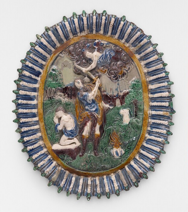 This is a painting of a scene with mythological or religious elements. The oval-shaped object is elaborately decorated with blue and white patterns, green accents, and detailed motifs. In the center, a figure kneels with bowed head and clasped hands, while another figure stands behind holding an object. An angelic figure emerges from clouds above, interacting with the scene. The background features lush greenery, trees, and a cityscape, with a small pot emitting flames. The style is reminiscent of Bernard Palissy.