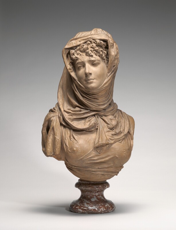 The head, shoulders, and upper chest of a woman are sculpted from light brown terracotta in this freestanding sculpture. In this photograph, the woman’s shoulders are angled very slightly to our right, and she turns and tips her head to look off to the left. She has a straight nose, full lips, and a dimpled chin. Fabric lies over curls piled atop her head and around her neck. Thin cloth drapes across her shoulders and chest, revealing one nipple. The bottom edge of the sculpture is curved, and the bust sits on a round, red stone base with molding at the top and bottom, and a tall, inward-curving cove around the center. The sculpture is photographed against a pale gray background.