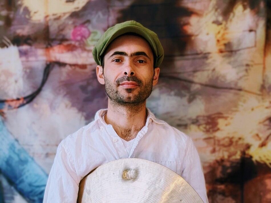 A man with a hat and a beard holding a cymbal.