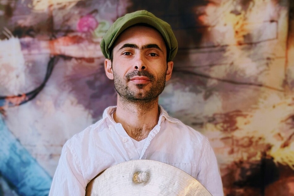 A man with a hat and a beard holding a cymbal.