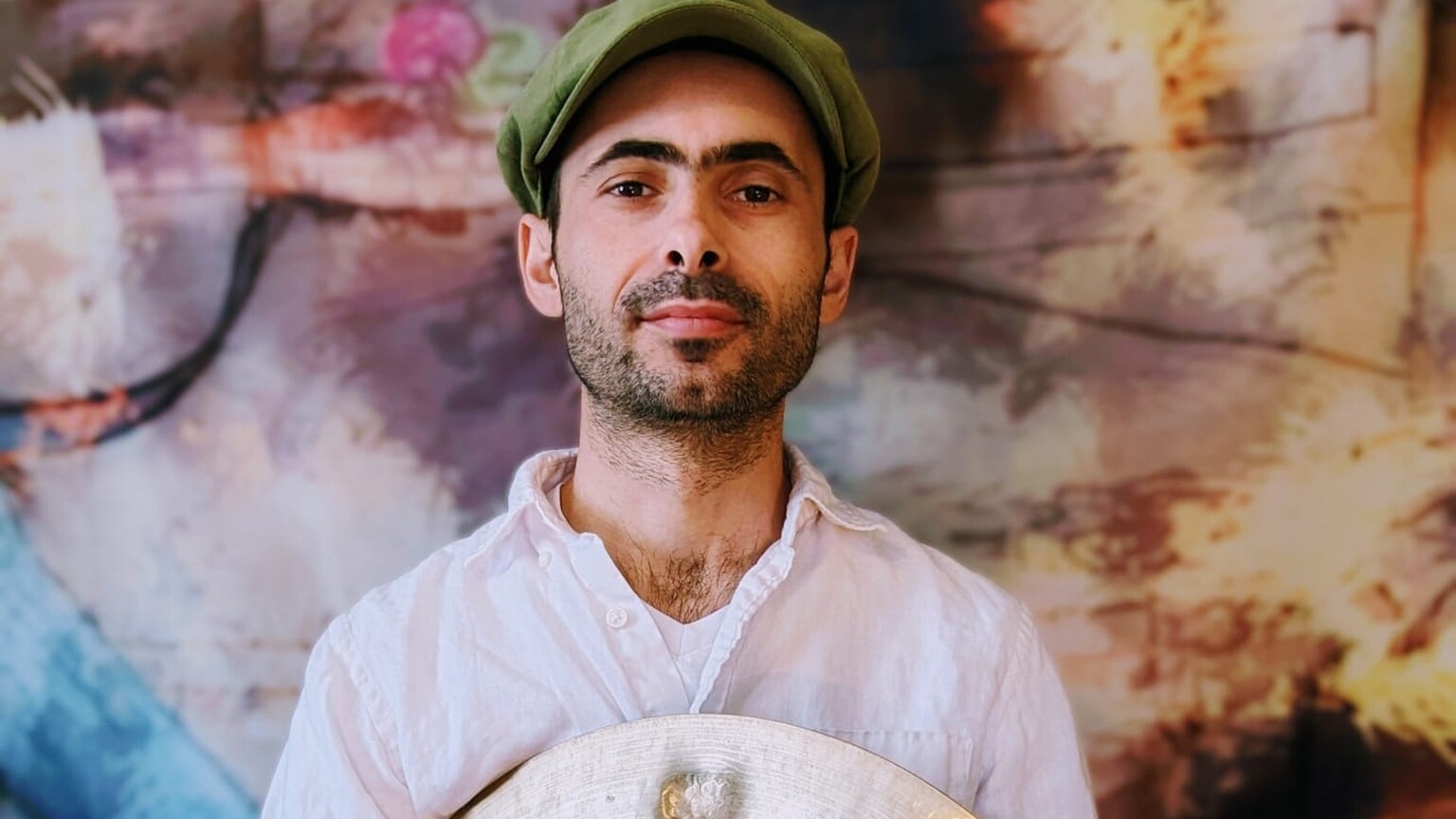 A man with a hat and a beard holding a cymbal.