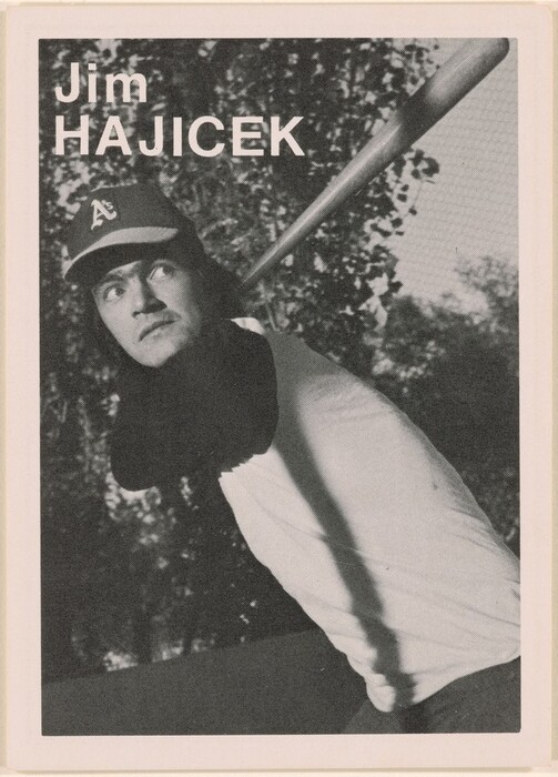 The image is a black and white photograph showing the upper body of a man positioned as if he is swinging a baseball bat. The individual is turned slightly to the side, with his head turned to the right. He has distinctive facial features, visible eyes, and medium-length hair peeking out from under a baseball cap. The cap features a visible logo, and the shirt he is wearing is a plain long-sleeved baseball tee with dark sleeves. He is holding a baseball bat across his shoulders. In the background, there are trees with leaves, creating a textured backdrop against the sky. The name "Jim Hajicek" is printed prominently in large, capitalized letters at the top left of the image.