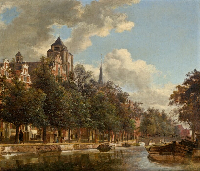 We look across a sunny waterway to the opposite bank, where a line of tall, leafy trees along the canal is backed by a row of red brick buildings and rowhouses with white stone trim in this horizontal landscape painting. The far bank angles from the lower left corner into the distance to our right, where it meets the horizon line near the right edge of the panel, about a fifth of the way up the composition.  The water in front of us ripples gently, reflecting the white clouds, pale blue sky, low barges or boats tied up along the edge of both sides of the canal, and the moss green of the trees. Tiny in scale, a few people walk and work under the trees along the far bank. The building closest to us, to our left, has a stepped roofline and a lantern-shaped cupola. The gray spire of a church rises above the trees farther down the canal, and more red brick buildings are visible in the gaps between the tree trunks. People and a horse cross a low, arched bridge spanning the canal in the distance to our right. The artist signed the painting as if he had inscribed his initials as a monogram on the boat closest to us to our right, “IVH.”