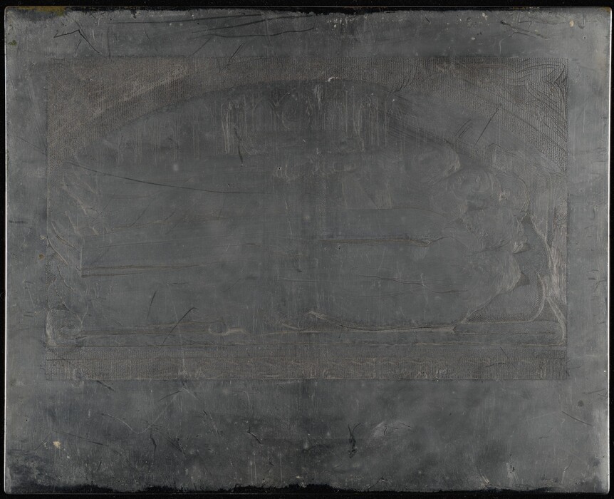 This is a photograph of an engraved metal plate. The plate has a worn and aged appearance, with scratches and areas of discoloration throughout. The design on the plate appears intricate, with various lines and textured areas. The edges of the plate are slightly beveled, and there is a visible border around the design.