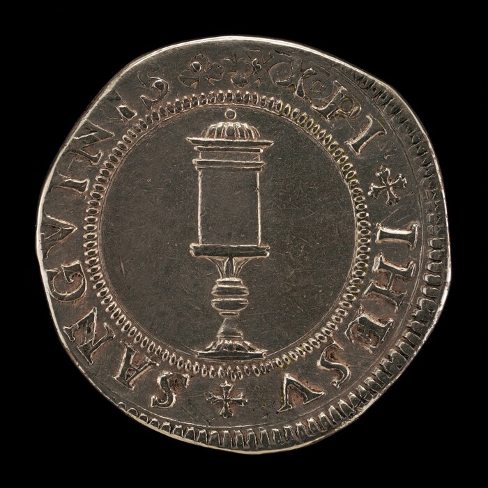 This is a photograph of an old coin. The coin features a central design of a cylindrical object resembling a pedestal or a column with a dome-shaped top, standing on a base. Surrounding the central motif is a circular border decorated with small beading. Encircling this area is engraved text, featuring phrases and decorative symbols that resemble stars. The text appears to be in an archaic script, potentially Latin or another classical language. The coin has a slightly irregular edge, indicating it may have been hand-struck or part of an ancient minting process.