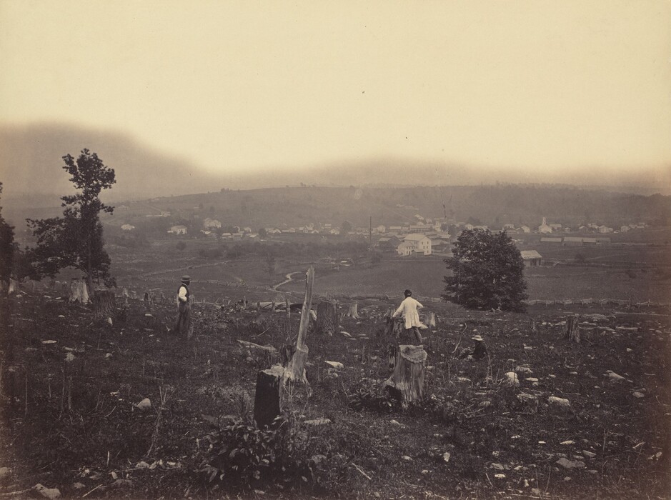 The image depicts a rural landscape with figures in a field with tree stumps and rocks. In the background, there is a hill, clouds, and a village with houses and a church steeple. The image appears to be in sepia tones, with a limited color palette of earthy browns and greys.