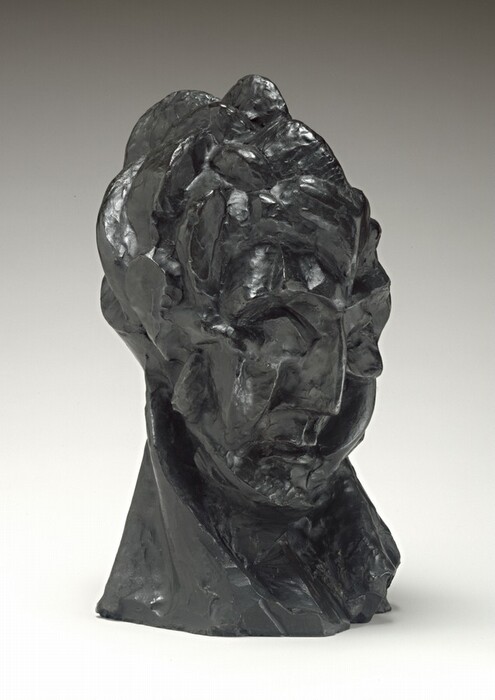 A woman’s face and neck are roughly modeled in this dark green, freestanding bronze sculpture. In this photograph, her face is angled to our right. She looks down, chin tucked back into her neck. She has deep-set eye sockets, a thin, blade-sharp nose, and her small mouth is closed, the corners downturned. Light from our left gleams off some of the surfaces, especially in the choppy hair and along the edge of her nose. A long diagonal ridge on the right side of her neck, our left, suggests a tendon stretching as she turns her head. Her neck acts as the sculpture's base. The background lightens from pale gray along the top to white along the bottom, where the sculpture casts a faint shadow to our right.