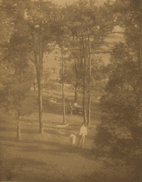 The image shows a park-like area from a slightly elevated perspective. Trees with elongated shadows cover the grassy ground. A man and a small child walk hand in hand. In the distance, a person sits on a bench partially hidden by trees. The horizon is blocked by dense foliage, with hints of a building visible. The scene is in sepia tone, giving it a vintage look. The textures have a brushstroke-like quality.