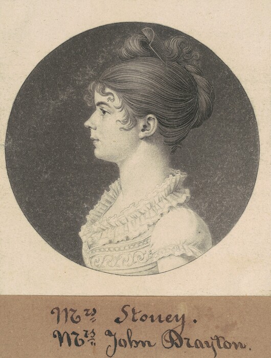 The image shows a profile portrait of a woman with a straight nose and defined lips. Her hair is in an updo with curls framing her face, and the back is neatly gathered. She wears a light-colored dress with lace and ruffle decorations. The background is shaded gray. Below the portrait, a hand-written inscription reads "Mrs. Stoney. Mrs. John Drayton."