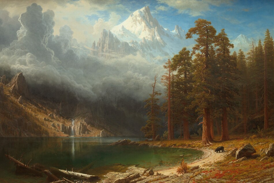 We look across the gleaming, forest-green surface of a lake at the foot of tall, jagged mountains in this horizontal landscape painting. The lake is flanked by a steep, gingerbread-brown hill on the left and a shoreline that forms a backward C curving from the lower center around and back along the right side of the composition. Strong sunlight from the upper left illuminates the center of the left-hand hill and the shoreline. The ground to our right is carpeted in rust-red, sage-green, and tan growth and is dotted with boulders. Tall trees with rust-brown trunks, crooked branches, and narrow canopies of caramel-brown and olive-green leaves fill the far end. Closest to us are dead tree trunks jutting out of the water and or lying on a flat, rocky outcropping nearby. Beyond the outcropping is a small black bear wandering down a sliver of sand-colored ground at the water’s edge. The hill on the left is covered with vertical rows of upright jagged boulders and slender, dark green trees marching up its slopes. A narrow, artic-blue waterfall cascades down its right side to empty into the lake. A thick layer of towering blue-gray clouds rises over the hill and lake, stretching back to the looming, snow-covered peaks that nearly brush the top edge of the canvas. The sky around the peak is vivid blue, scattered with high white clouds. The artist signed the lower right, “ABierstadt” with the A and B joined as a monogram.
