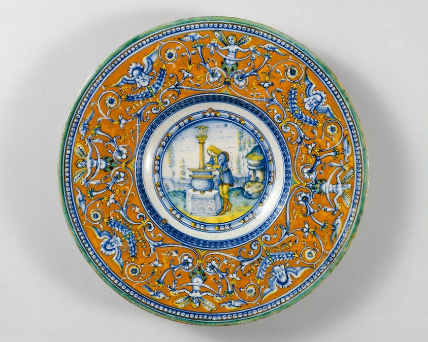 Plate with border of grotesques on an orange ground; in the center, Narcissus gazing at his reflection in a fountain