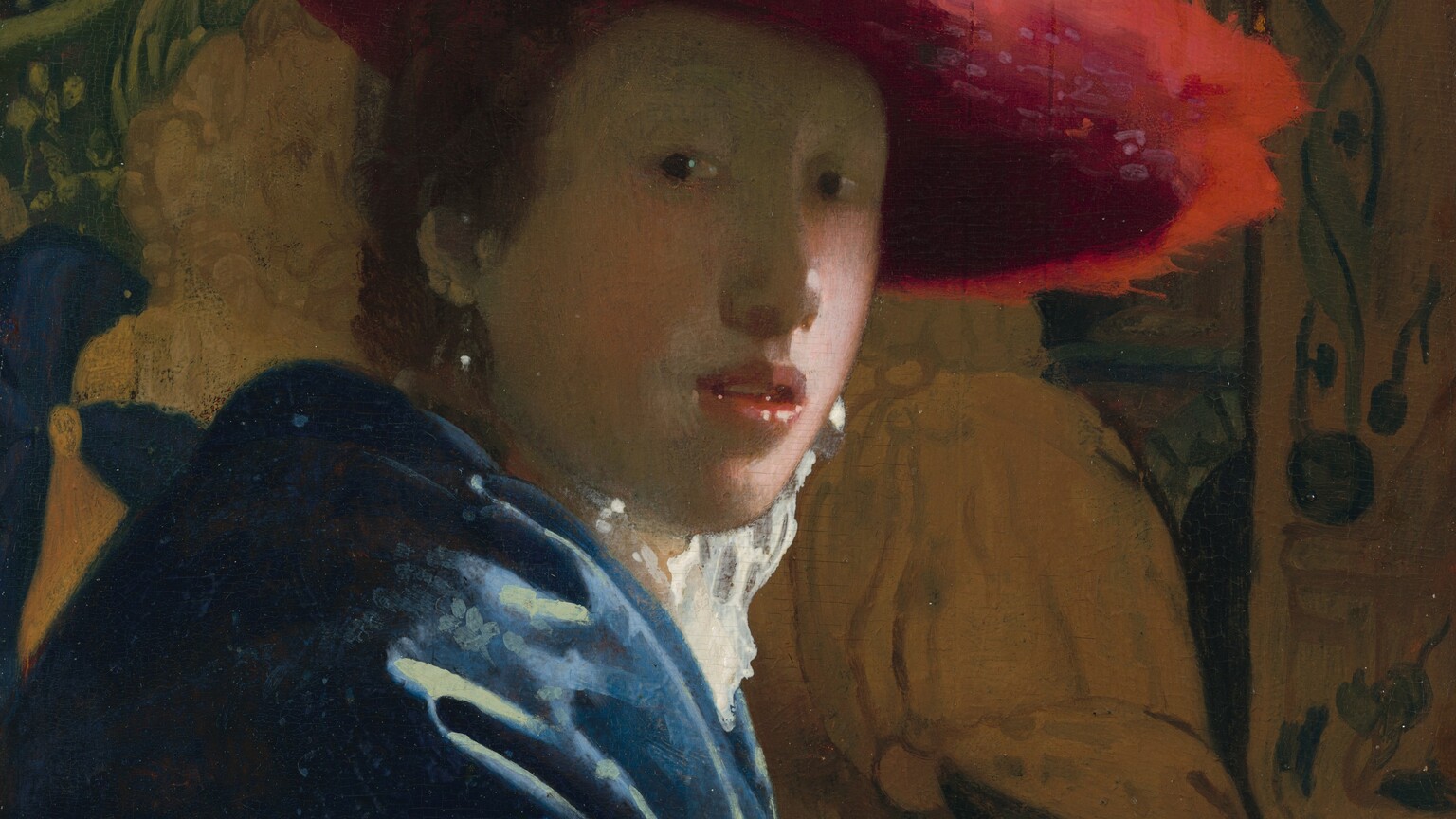 Shown from the elbows up, a young person with pale skin and brown hair wearing a wide, scarlet-red hat sits in front of a tapestry in this vertical portrait painting. She sits with her body facing our right in profile but she turns her face to look at or toward us with dark eyes. She has a rounded nose, rather flat cheeks, and a sliver of teeth is visible through parted coral-pink lips. The wide brim of the red hat seems to be made of a soft, almost feathery material, and it casts a shadow across her face. She wears a high-collared white garment that catches the light, a royal-blue, possibly velvet, robe or overcoat, and large, teardrop pearl earrings. Her arm runs along the bottom edge of the panel in front of two carved, wooden lion finials that could be the arm or back of the chair. The tapestry behind her is painted in tones of pale caramel brown and pine green. The painting has a soft, hazy look, and light glints with bright white specks off the pearl earrings, the tip of her nose, her lips, and the lion finials.