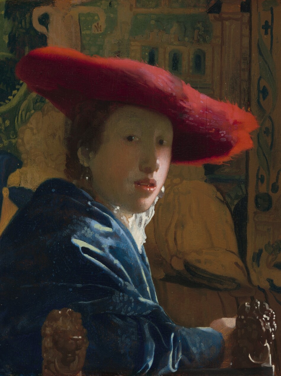 Shown from the elbows up, a young person with pale skin and brown hair wearing a wide, scarlet-red hat sits in front of a tapestry in this vertical portrait painting. She sits with her body facing our right in profile but she turns her face to look at or toward us with dark eyes. She has a rounded nose, rather flat cheeks, and a sliver of teeth is visible through parted coral-pink lips. The wide brim of the red hat seems to be made of a soft, almost feathery material, and it casts a shadow across her face. She wears a high-collared white garment that catches the light, a royal-blue, possibly velvet, robe or overcoat, and large, teardrop pearl earrings. Her arm runs along the bottom edge of the panel in front of two carved, wooden lion finials that could be the arm or back of the chair. The tapestry behind her is painted in tones of pale caramel brown and pine green. The painting has a soft, hazy look, and light glints with bright white specks off the pearl earrings, the tip of her nose, her lips, and the lion finials.