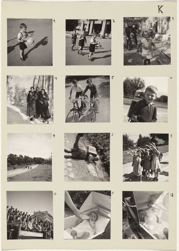 Square black and white photographs are arranged in a grid of four rows and three columns on cream-white paper and numbered 1 through 12. Most photographs show one, a pair, or small groups of children, all of whom appear to have pale skin. Number 1 is of a small boy wearing a collared shirt, black shorts, and shiny black shoes playing a toy drum hung around his neck. In number 2, two more boys march in a line down a town street following the drummer. At the top right of the page, number 3 shows a girl in dappled sunlight holding the hem of her dress out as two adults smile in the blurry background. In the next row, number 4 is of three older boys smiling and standing on a snowy hill. The middle boy has his arms around the shoulders of the other two, and the boy to our right holds that hand. Number 5 is of two older boys wearing shorts and collared shirts on bicycles on a dirt path. Next, a boy wearing a sweater smiles at the camera, both front teeth missing. About a dozen kids run toward us from a distance on a dirt path in number 7, and a boy with a boxy knapsack lies on the dirt ground to inspect something down an incline in number 8. Then seven young girls stand closely in a pack and smile widely as they point up and to our left in number 9. Number 10 shows more than fifty kids sitting on bleachers, and the final two, numbers 11 and 12, show a baby being fed a bottle in a stroller.