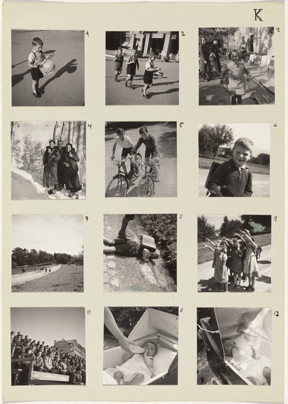 Square black and white photographs are arranged in a grid of four rows and three columns on cream-white paper and numbered 1 through 12. Most photographs show one, a pair, or small groups of children, all of whom appear to have pale skin. Number 1 is of a small boy wearing a collared shirt, black shorts, and shiny black shoes playing a toy drum hung around his neck. In number 2, two more boys march in a line down a town street following the drummer. At the top right of the page, number 3 shows a girl in dappled sunlight holding the hem of her dress out as two adults smile in the blurry background. In the next row, number 4 is of three older boys smiling and standing on a snowy hill. The middle boy has his arms around the shoulders of the other two, and the boy to our right holds that hand. Number 5 is of two older boys wearing shorts and collared shirts on bicycles on a dirt path. Next, a boy wearing a sweater smiles at the camera, both front teeth missing. About a dozen kids run toward us from a distance on a dirt path in number 7, and a boy with a boxy knapsack lies on the dirt ground to inspect something down an incline in number 8. Then seven young girls stand closely in a pack and smile widely as they point up and to our left in number 9. Number 10 shows more than fifty kids sitting on bleachers, and the final two, numbers 11 and 12, show a baby being fed a bottle in a stroller.