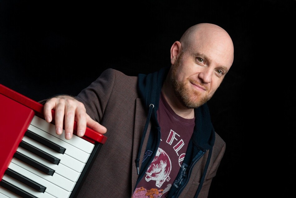 A bald man with a beard standing next to a keyboard.