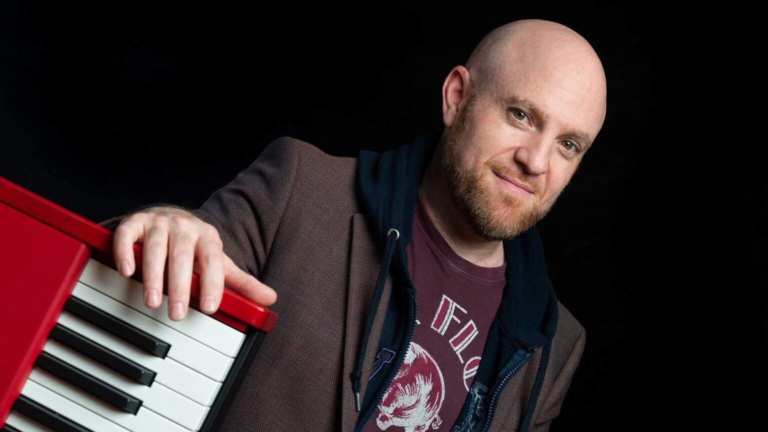 A bald man with a beard standing next to a keyboard.