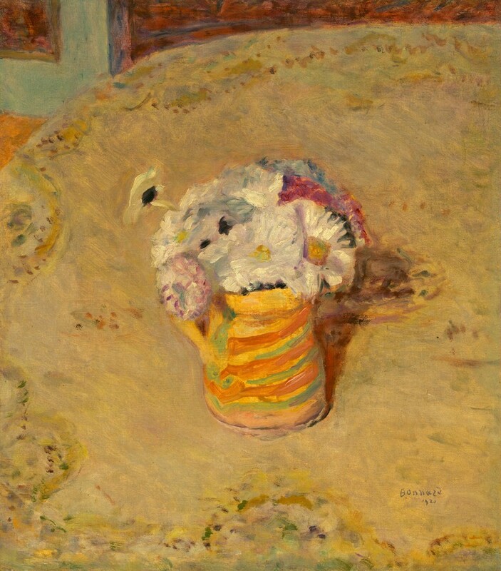 We look down onto pitcher holding mostly white flowers on a tabletop in this loosely painted, vertical still life. The white flowers have yellow centers, and a few darker pink and blue flowers are at the back of the bouquet. The pitcher is striped almost horizontally with harvest yellow, lime green, and pumpkin orange. The tabletop nearly fills the picture, and the cloth is painted as a field of straw yellow edged with a pattern suggested with touches muted green, violet purple, and burgundy red. A sliver of the floor and room beyond the table is visible along the top edge of the canvas. Areas of seafoam blue, marigold orange, and rust red suggest the corner of a door on a carpet. The artist signed and dated the lower right corner, “Bonnard 1920.”