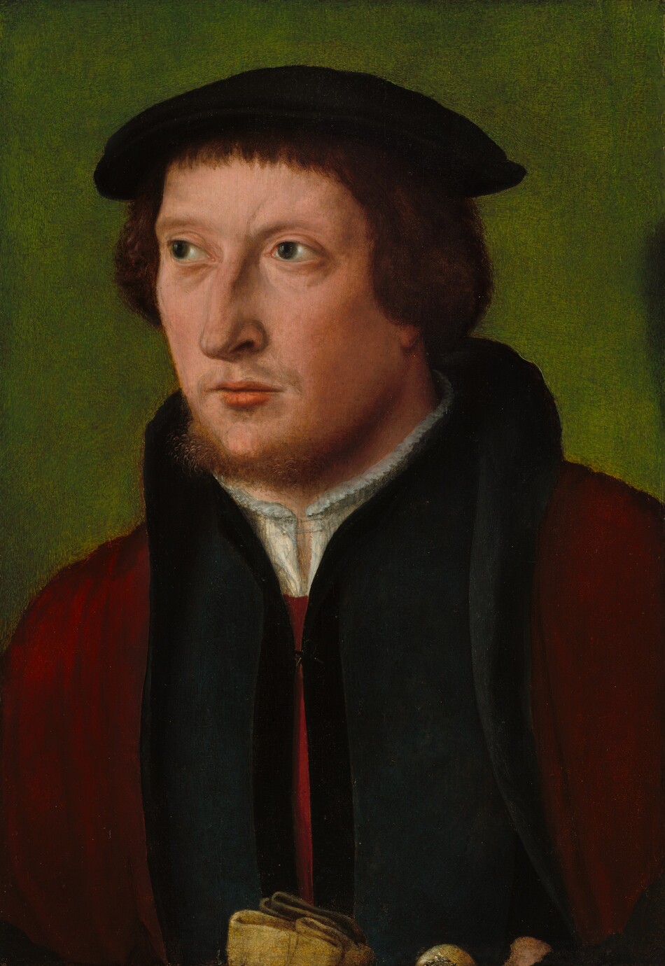 The image depicts a man from the waist up, positioned in a three-quarter view as he looks to his left. He has a fair complexion, a reddish-brown close-cropped beard, and medium brown hair cut at ear length. He wears a black flat cap, a white undershirt, a deep blue or black coat, and a burgundy overcoat draped over his shoulders. He is holding an object in his hands. The background is a muted olive green color.