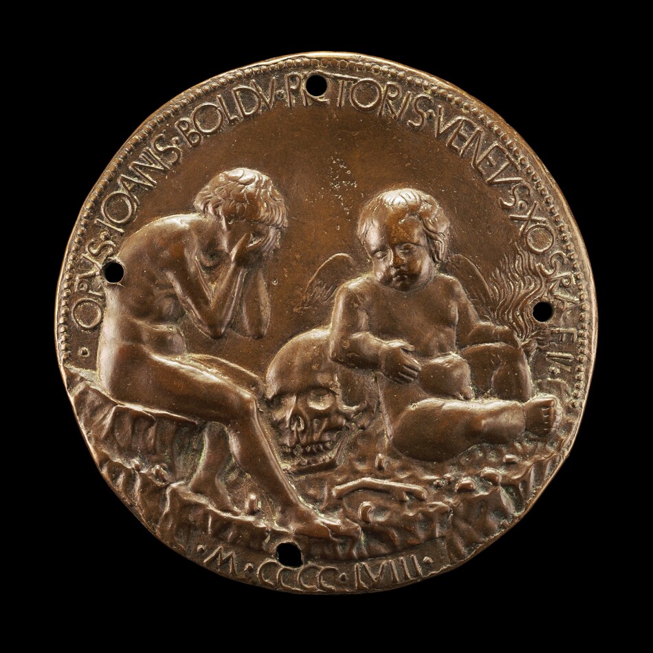 The sculpture is a round bronze relief depicting two cherubic figures seated on the ground. One figure covers their face with one hand, while the other holds a human skull. Both figures have youthful features and subtle musculature. The background contains ornate lines, and the sculpture is bordered with a Latin inscription. The material is polished bronze, giving the sculpture a rich brown color with lighter highlights. The viewer sees details of the figures' expressions and the crafting of the skull, highlighting the skillful work in small-scale bronze artistry.