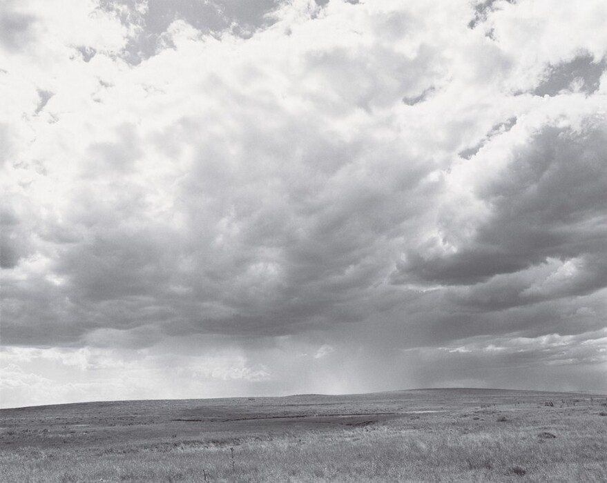 The image shows a landscape with a horizon line in the lower third of the composition. The grassland below is separated from the cloudy sky above. The sky is filled with thick, layered grey and white clouds, suggesting stormy weather. The brushstrokes create a sense of depth and movement. The color palette is monochromatic with various shades of grey. The land appears flat and extends towards the horizon.