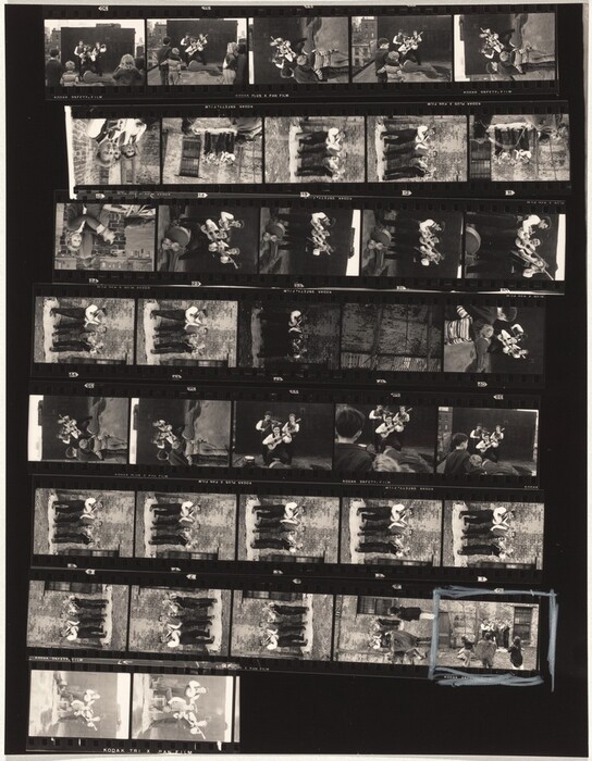 This is a photograph of a contact sheet. The image contains multiple small black-and-white photographs arranged in a grid. These images showcase various scenes set against an urban backdrop, with different compositions and angles. The photographs appear to capture dynamic and informal moments. Each portion of the contact sheet provides a slice of life, with a blue marking highlighting one of the frames. The film details and frame numbers are visible around the borders of each series of images.