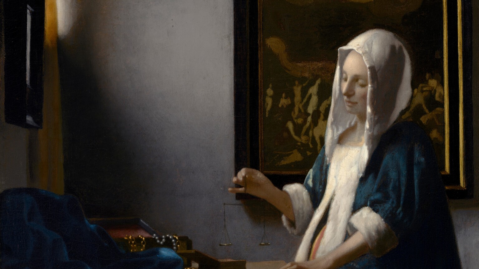 In this vertical painting, a woman stands near the corner of a dimly lit room, facing our left in profile and looking down at a balance she holds suspended in her right hand over a wooden table. She wears a peacock-blue velvet jacket with a white hood and fur lining, and a voluminous, mustard-yellow skirt. A window near the upper left corner is partially covered by a canary-yellow curtain. Light coming in through that window falls on the pale skin of the woman's face and hands, and highlights the white trim of her garment. Her left hand, closer to us, rests on the edge of the table near two open boxes, and a blue cloth is bunched at the back of the table to our left. Gold chains and pearl strands drape over the edge of one box. The woman stands in front of a framed painting. Much of the detail is lost in shadow but at the top center of the painting, a person surrounded by a golden halo floats in the sky with both arms raised, and is flanked by people encased within a bank of clouds. Nude people on the ground below in the painting, seen to either side of the woman, writhe, twist, and point upward.