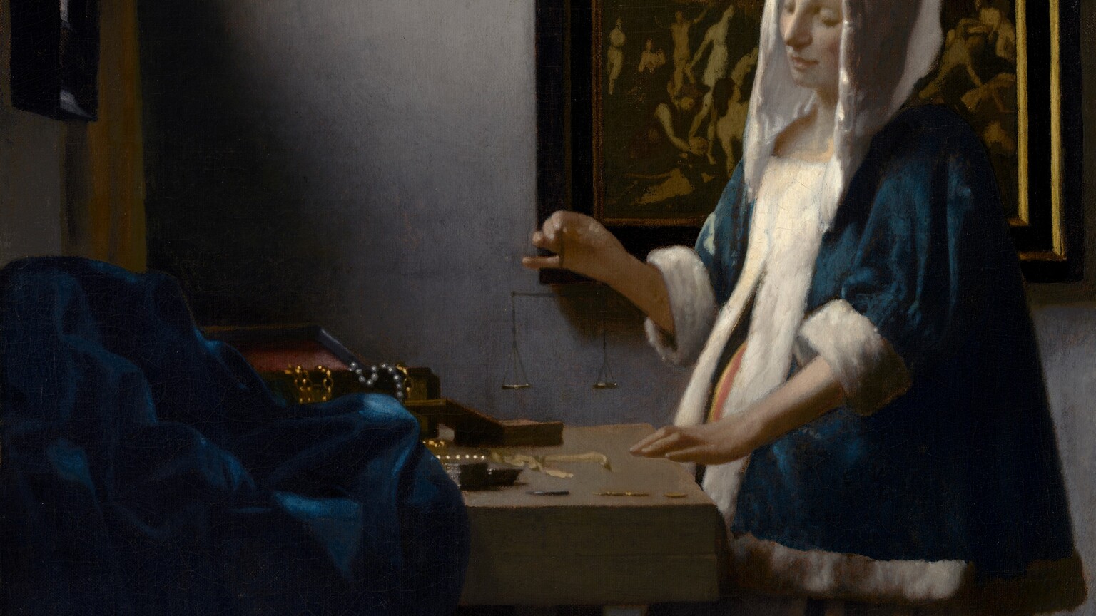 In this vertical painting, a woman stands near the corner of a dimly lit room, facing our left in profile and looking down at a balance she holds suspended in her right hand over a wooden table. She wears a peacock-blue velvet jacket with a white hood and fur lining, and a voluminous, mustard-yellow skirt. A window near the upper left corner is partially covered by a canary-yellow curtain. Light coming in through that window falls on the pale skin of the woman's face and hands, and highlights the white trim of her garment. Her left hand, closer to us, rests on the edge of the table near two open boxes, and a blue cloth is bunched at the back of the table to our left. Gold chains and pearl strands drape over the edge of one box. The woman stands in front of a framed painting. Much of the detail is lost in shadow but at the top center of the painting, a person surrounded by a golden halo floats in the sky with both arms raised, and is flanked by people encased within a bank of clouds. Nude people on the ground below in the painting, seen to either side of the woman, writhe, twist, and point upward.