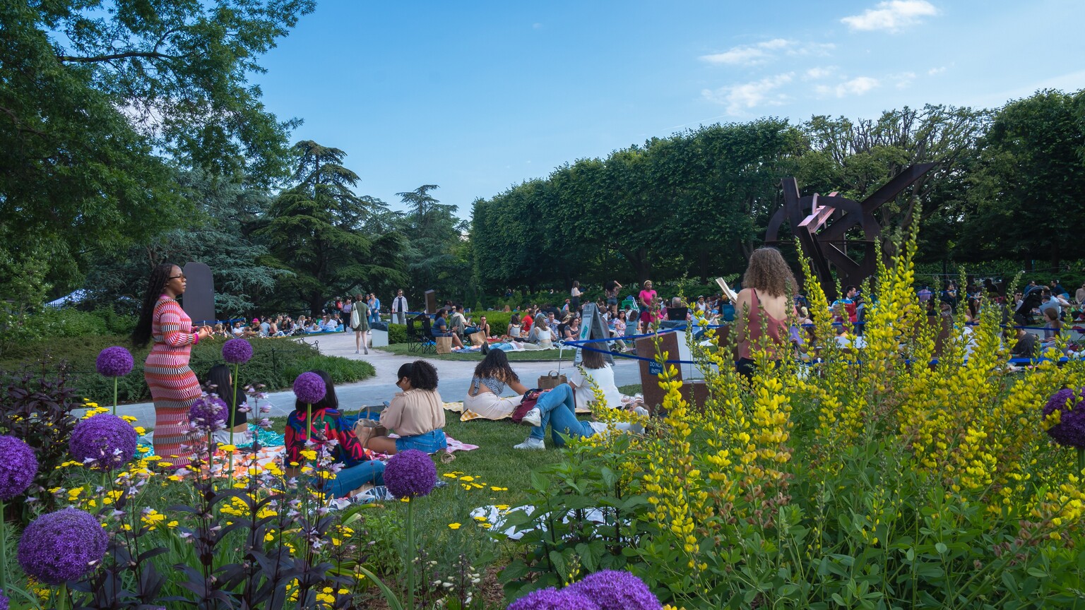 People standing, sitting, and walking around in the Sculpture Garden during a Jazz in the Garden event.