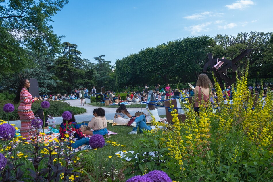 People standing, sitting, and walking around in the Sculpture Garden during a Jazz in the Garden event.