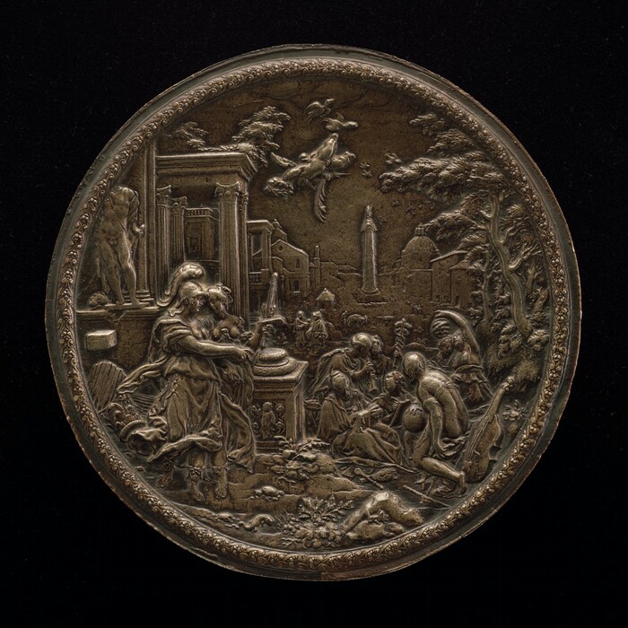 The sculpture is a relief depicting a classical scene with various figures in an outdoor setting. The central figures are gathered around a table or altar, with two women in the foreground, one holding a mirror and the other seated. Other figures are engaged in different activities behind them, including sitting and standing. Animals, such as a flying bird, are depicted above. The background includes architectural elements like columns, along with a landscape featuring trees and distant buildings. The circular sculpture is made of a material resembling bronze, giving it a metallic brown appearance. The relief is highly detailed with intricate carvings, reflecting inspiration from classical art.