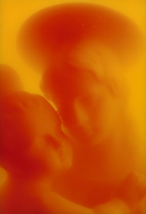 The hazy, unfocused faces of a woman and baby and their halos fill this vertical composition, which is printed in tones of tangerine orange and goldenrod yellow. The woman and child are almost cheek to cheek, with the child to the left and woman to the right. The outlines are blurred, giving the print an ethereal, otherworldly look.