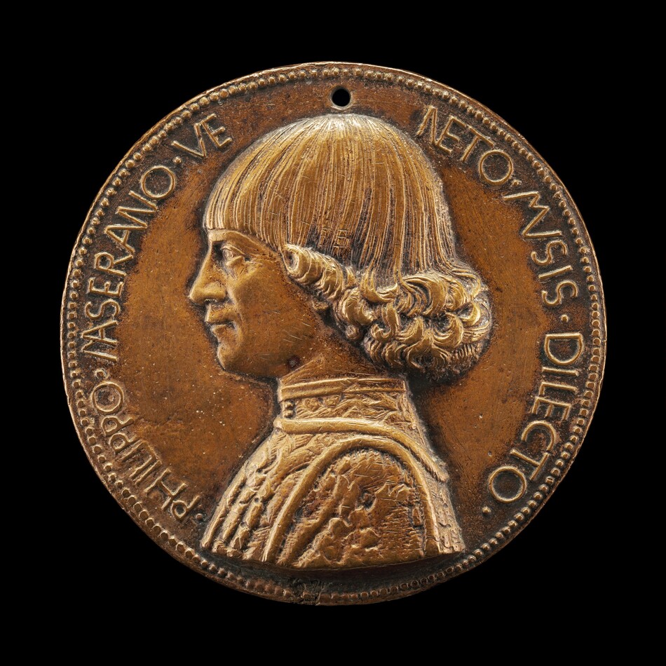 The image shows a sculptural medallion with a profile of a man with distinctive wavy hair styled into a bob, adorned with intricately carved curls. He is dressed in a detailed garment with decorative patterns around the collar. The medallion is a warm brown color, suggesting it is made of bronze or a similar metallic material. The outer edge of the medallion has an inscription. The medallion is relatively small and has a hole at the top.