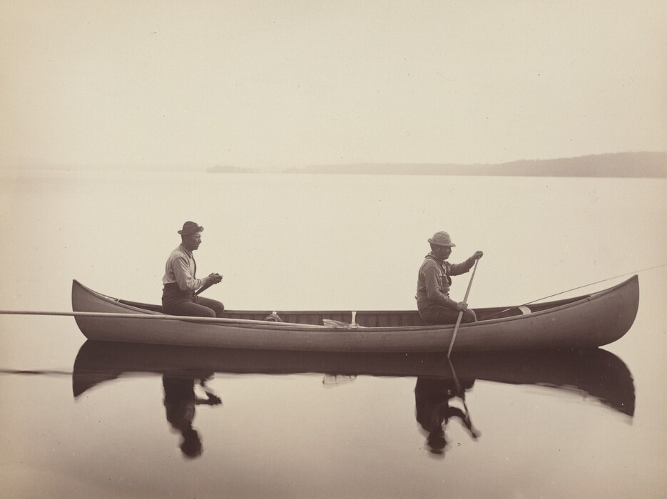 The image shows a canoe on a calm body of water with two individuals inside. The canoe is centered with perfect symmetry, and its reflection is visible in the water. The horizon is low with a faint line suggesting distant land. The photograph is in sepia tones, giving it a vintage aesthetic dominated by shades of brown and beige. The transition between water and sky creates a serene atmosphere.