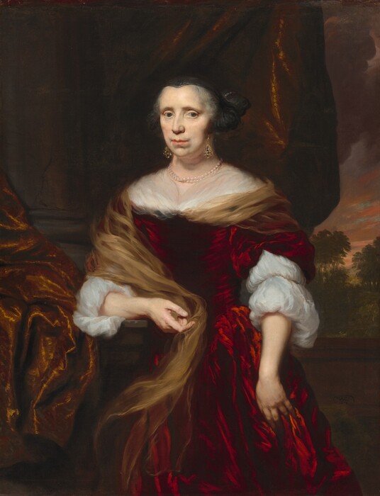 Shown from the knees up, a pale-skinned woman with gray hair and wearing a scarlet-red, velvet dress looks at us in this vertical portrait painting. The woman’s shoulders and face are angled slightly to our left so she gazes out of the corners of her dark blue eyes under sloping brows. Her pink lips are closed, and jowls soften her chin line. She wears a black cap over her gray hair, and gold, jeweled earrings hang from her ears. A double strand of pearls is around her neck. The bodice of her dress is cut straight across the shoulders, and white cloth covering her decolletage is tucked into the neckline. A muted gold cloth wraps around the woman’s left shoulder, to our right, across her back, and down over her other elbow. The red dress’s sleeves split over the puffy white sleeves of her undergarment. The woman rests her right elbow, to our left, on a ledge, and her other hand hangs by her side with those fingers nestled into the fabric of her skirt. An iridescent, gold-colored cloth drapes over the ledge to our left and behind the woman. A stone column is along the left edge of the painting and a sunset sky over a grassy, tree-filled landscape is visible to the right. The artist signed and dated the lower right corner, “NMaes 1676.”