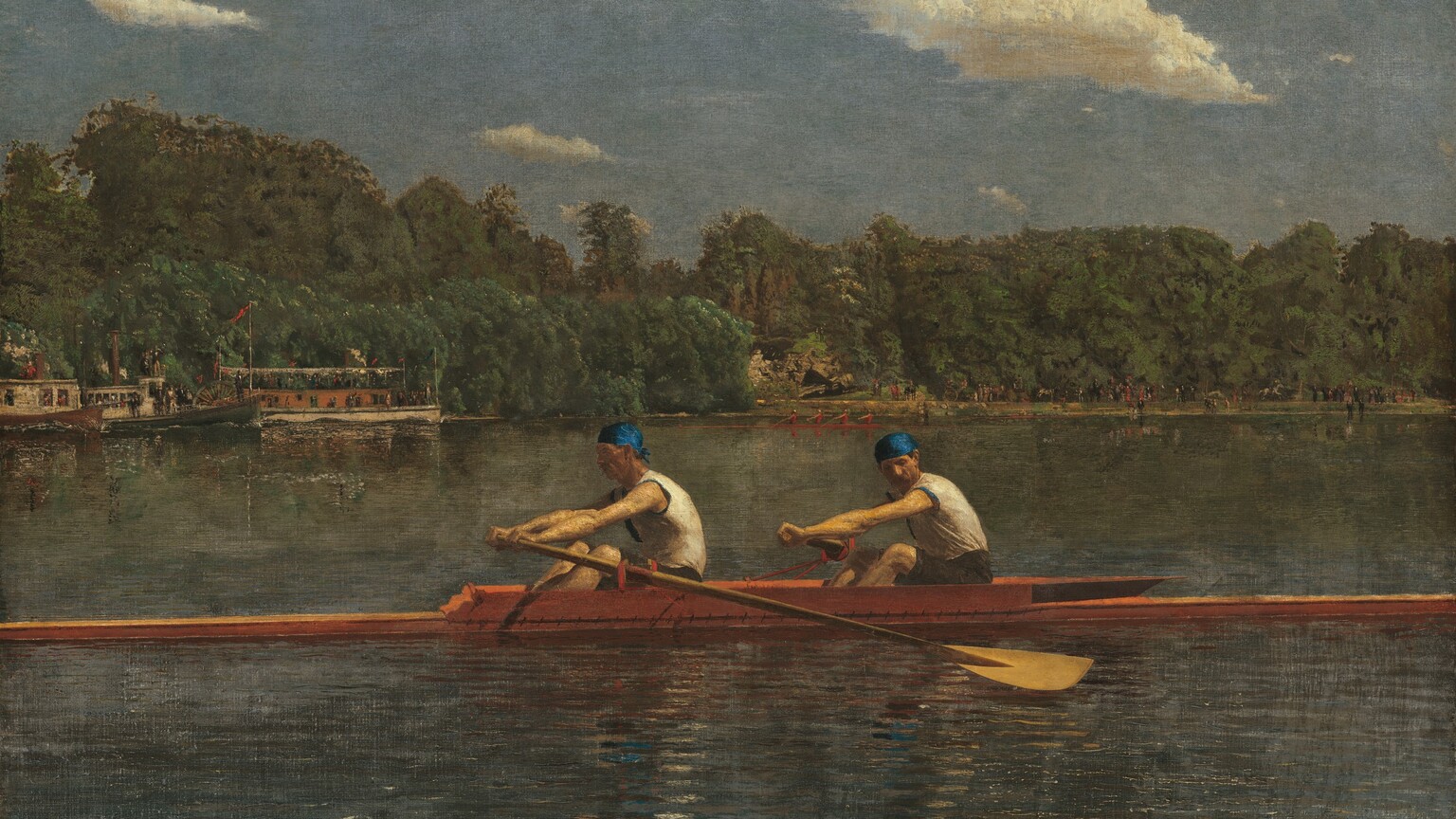 Two men with pale skin, wearing white sleeveless shirts and royal-blue caps, row in unison in a long, narrow boat on a placid blue river in this horizontal landscape painting. The low, honey-colored wooden boat extends off both sides of the canvas. Both men face our left as they row to our right. The man in front looks ahead of him, beyond the stern of the boat, and the man to our right, closer to the bow, tucks his chin down to look past his shoulder. Their bare, muscled arms are extended straight as the two oars sweep back. The tip of another boat runs close and parallel to the bottom edge of the composition, spanning the left three-quarters of the painting. The opposite riverbank is lined with a dense forest of pine-green trees. People crowd along the decks of a steamboat and a paddleboat near the riverbank to our left. Another narrow skuller, rowed by four people wearing ruby-red shirts, cuts through the water at the back center of the river. The riverbank beyond is lined with people, painted with strokes of black and white, and minuscule touches of red. The horizon comes halfway up the composition. Cream-white clouds float across a muted, topaz-blue sky above the trees.